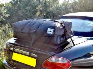 black jaguar xk8 convertible with a boot-bag vacation luggage rack fitted next to a bush on a sunny day
