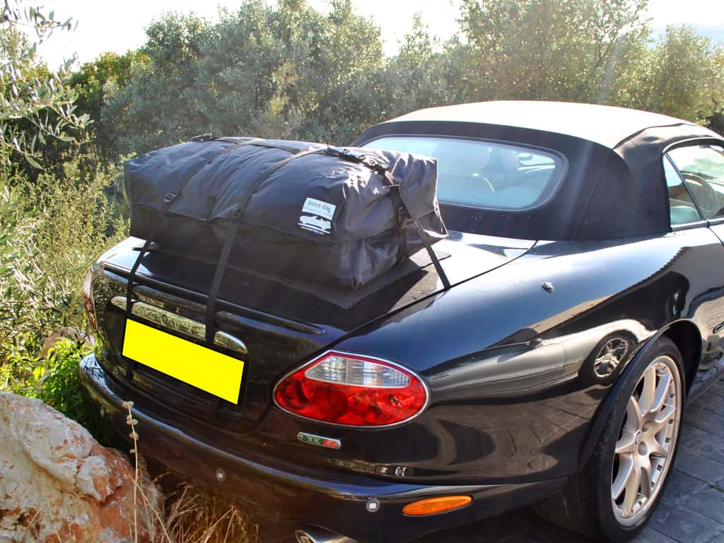 black jaguar convertible next to a wooded area hood up with a luggage rack fitted