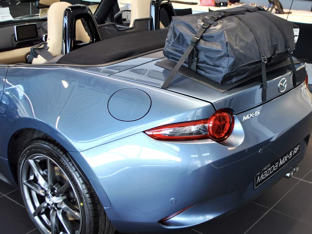 side view of a blue mazda mx5 mk4 miata nd with a boot-bag original luggage rack fitted in a mazda showroom