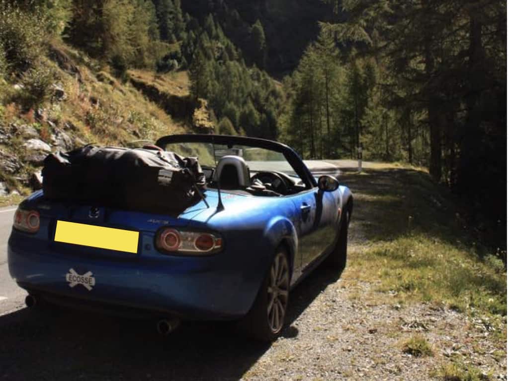 blue mazda mx5 mk3 miata nc on a hilly road hood down with a boot-bag vacation luggage rack fitted