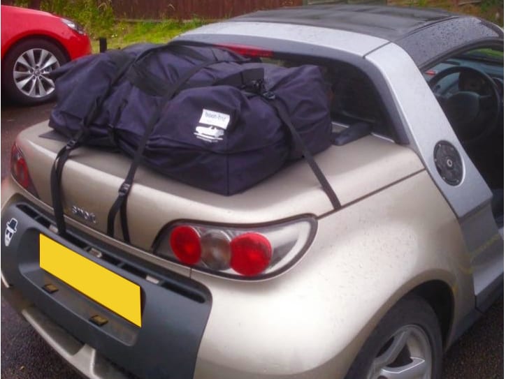 gold smart roadster with a boot-bag vacation luggage rack fitted in a car park on a rainy day