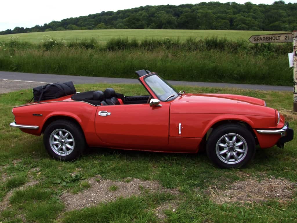 red triumph spitfire hood down on a green with a boot-bag original luggage rack fitted photographed from the side
