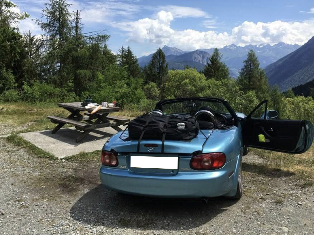 blue mazda mx5 mk2 with a boot-bag luggage rack fitted next to a picnic table overlooking a large valley