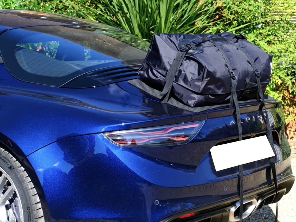 blue alpine a110 with a boot-bag luggage rack fitted next to a hedge