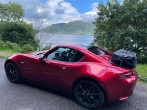 red mx5 rf with a boot rack fitted next to a tree by a lake