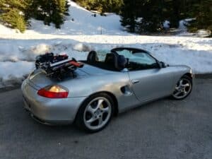 silver porsche boxter 986 with the roof down next to snow and a luggage rack fitted carrying skis