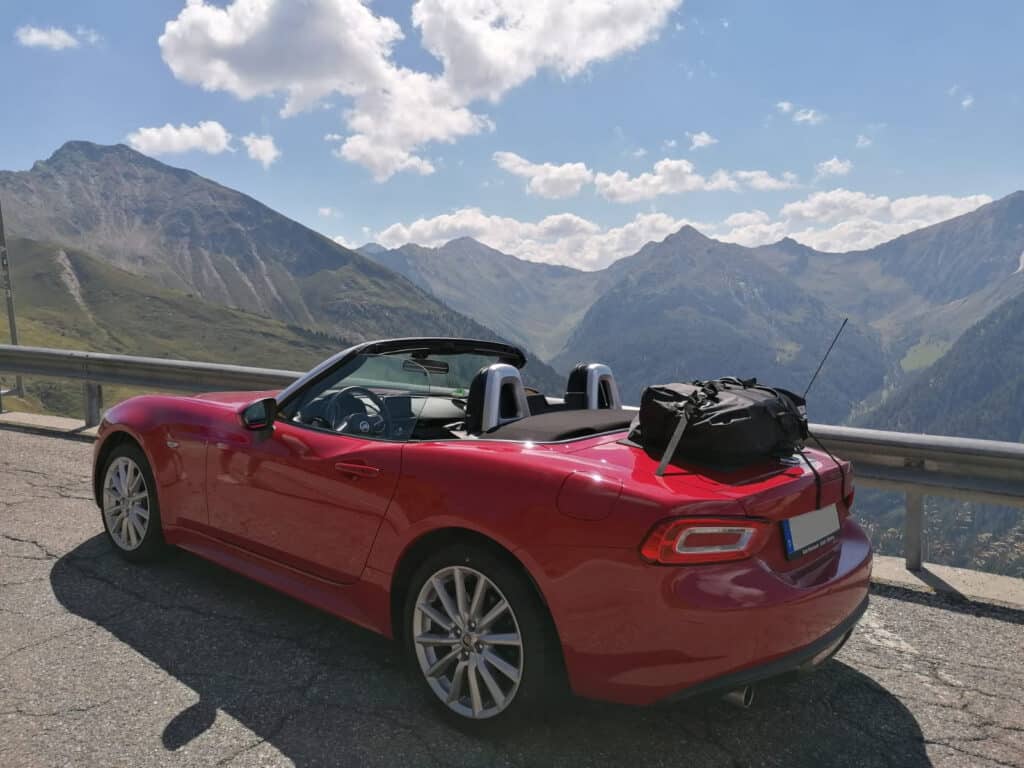 red fiat 124 spider with a boot-bag luggage rack fitted on a mountain road