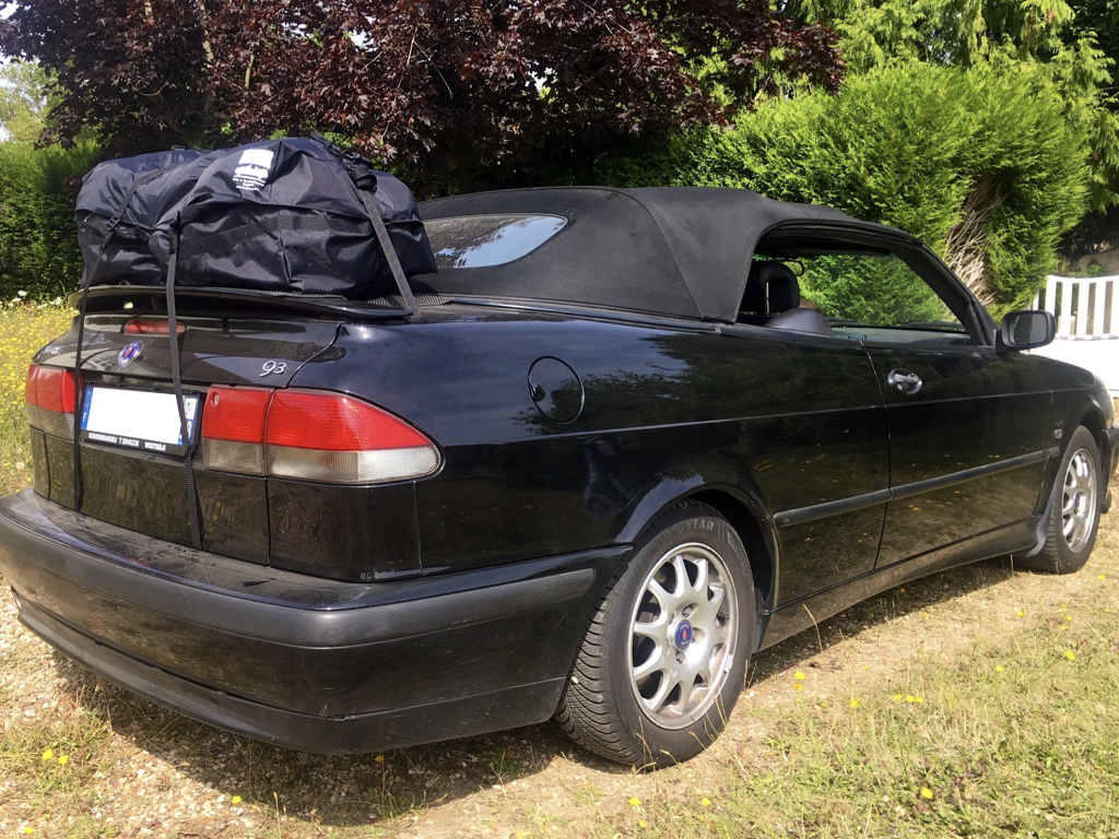 black saab 93 convertible with a boot-bag vacation luggage rack fitted in a field on a sunny day