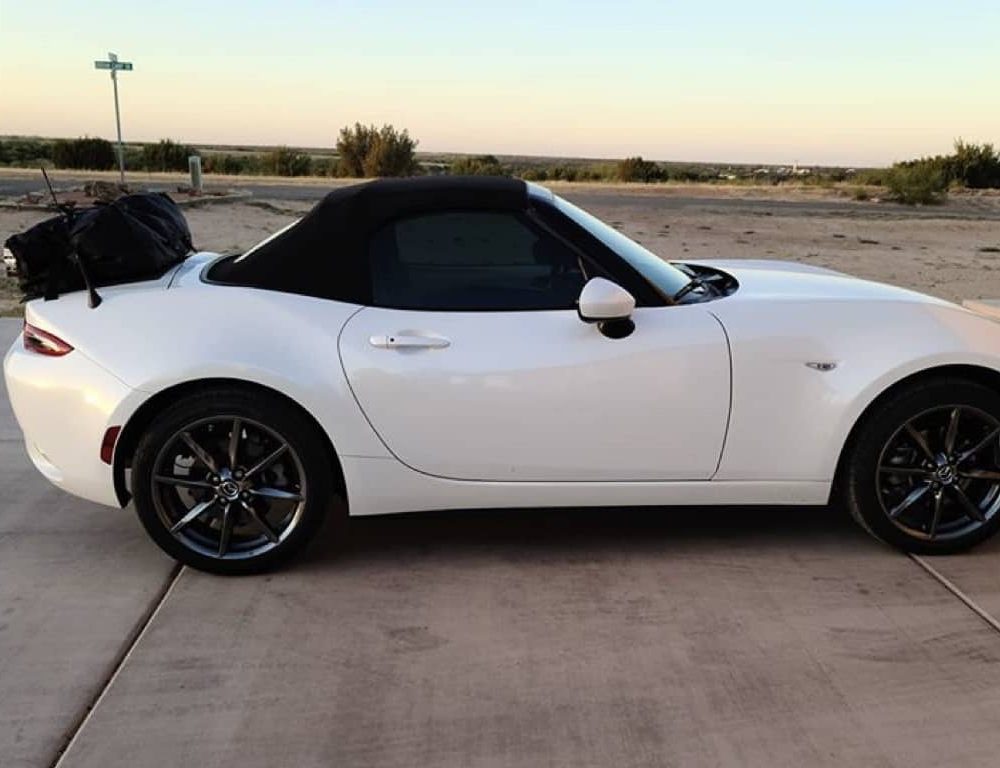white mazda miata mx5 nd with a boot-bag luggage rack fitted photographed from the side in the desert.
