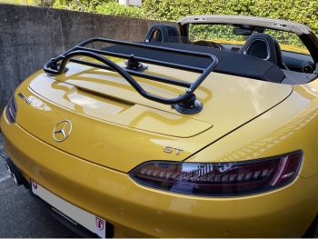 Mercedes amg gtc roadster jaune avec le toit baissé et un porte-bagages noir monté photographié de derrière lors d'une journée ensoleillée