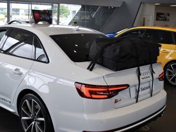 white audi s4 a4 sedan in an audi dealership showroom with a boot-bag roof box luggage carrier alternative fitted to the trunk lid photographed from the rear