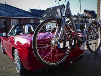 Rosso fiat 124 spider al di fuori di una casa in una giornata di sole con un portabiciclette montato che trasporta una bicicletta