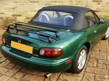 green mazda mx5 na with a black luggage rack fitted photographed close at the rear by a wall