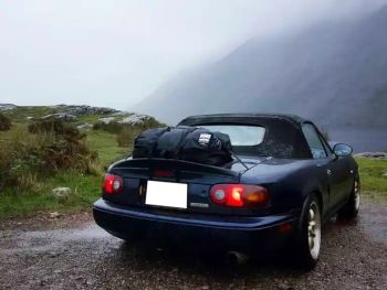 niebieska Mazda MX5 NA z bagażnikiem zamontowanym od tyłu na mglistym szczycie wzgórza w deszczu