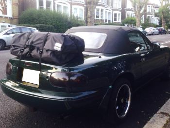 green mazda mx5 mk1 with a boot-bag vacation luggage rack fitted in a residential street