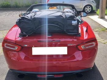 Rode Fiat-spin met een waterdichte bagagetas met koffer, vastgebonden aan een bagagerek, vlak aan de achterkant gefotografeerd